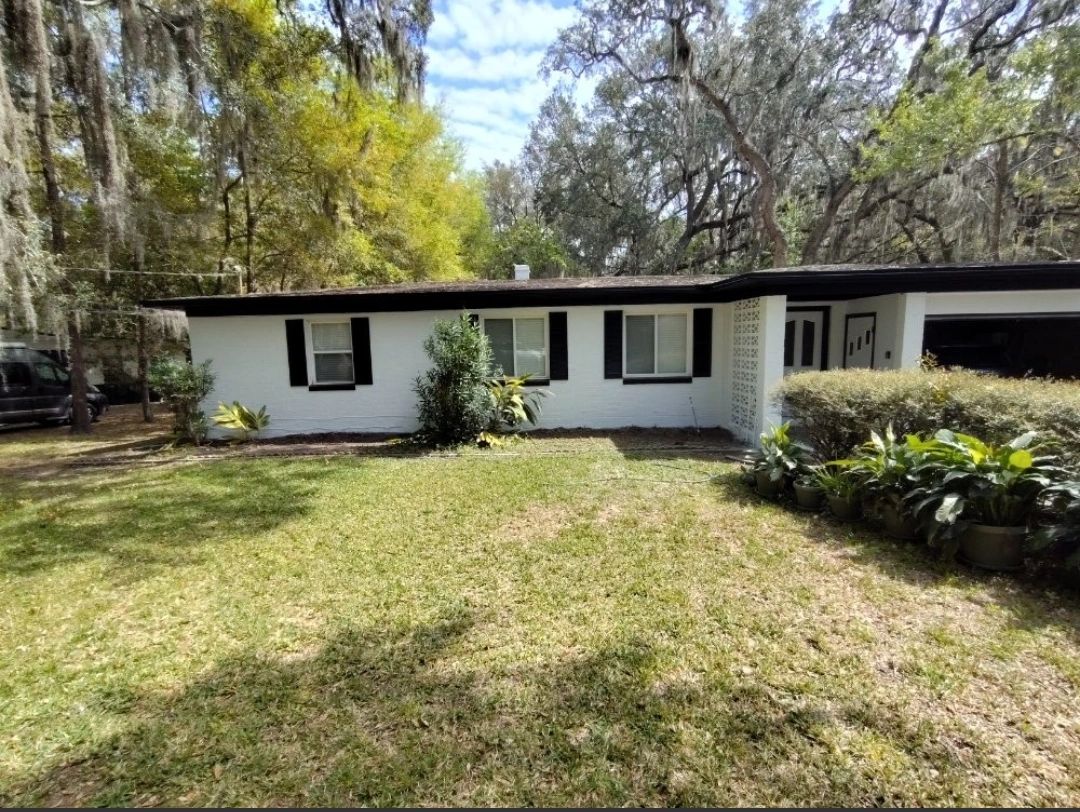 A white house with black shutters and trees in the background