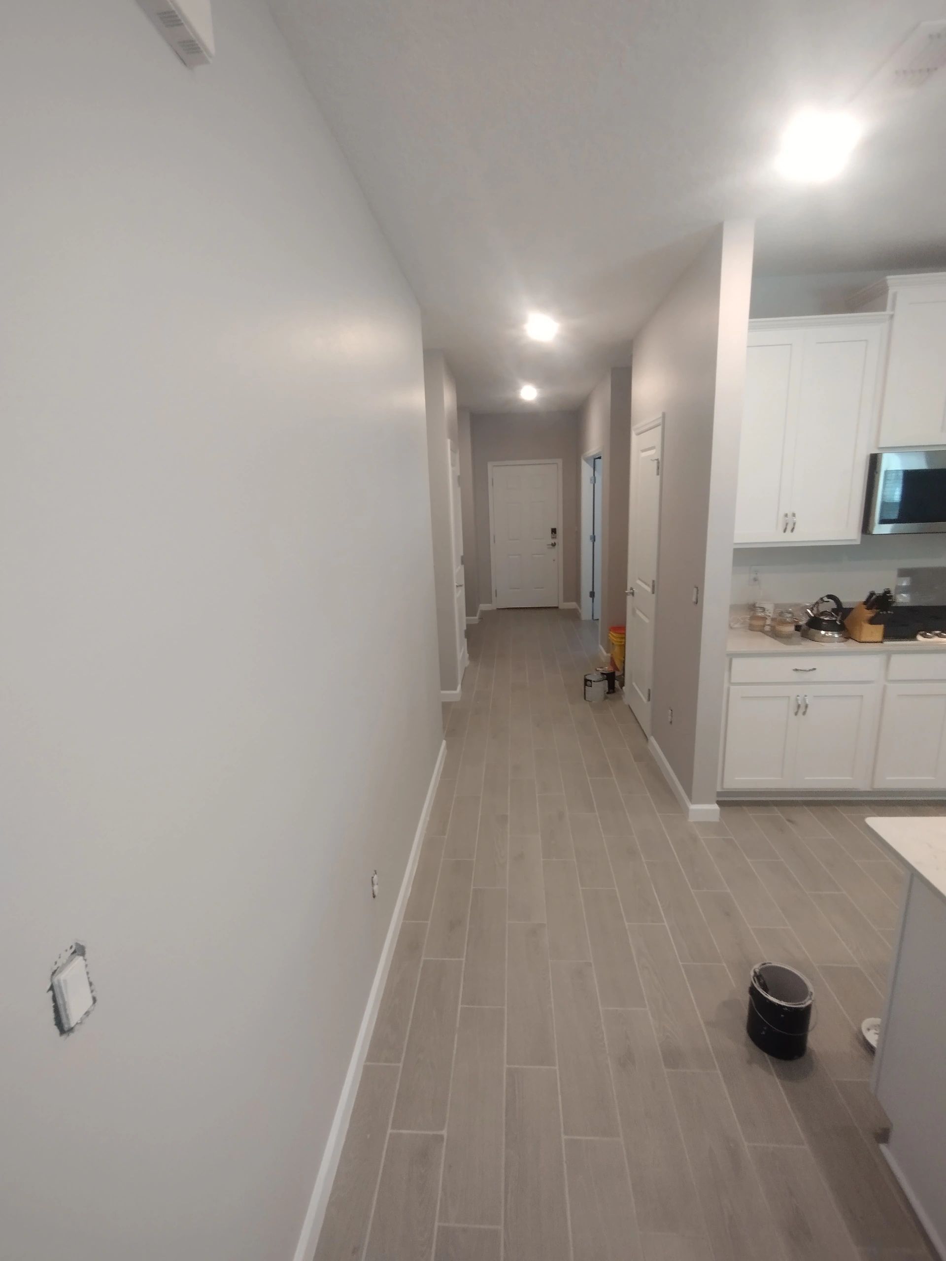 A long hallway with white cabinets and wood flooring